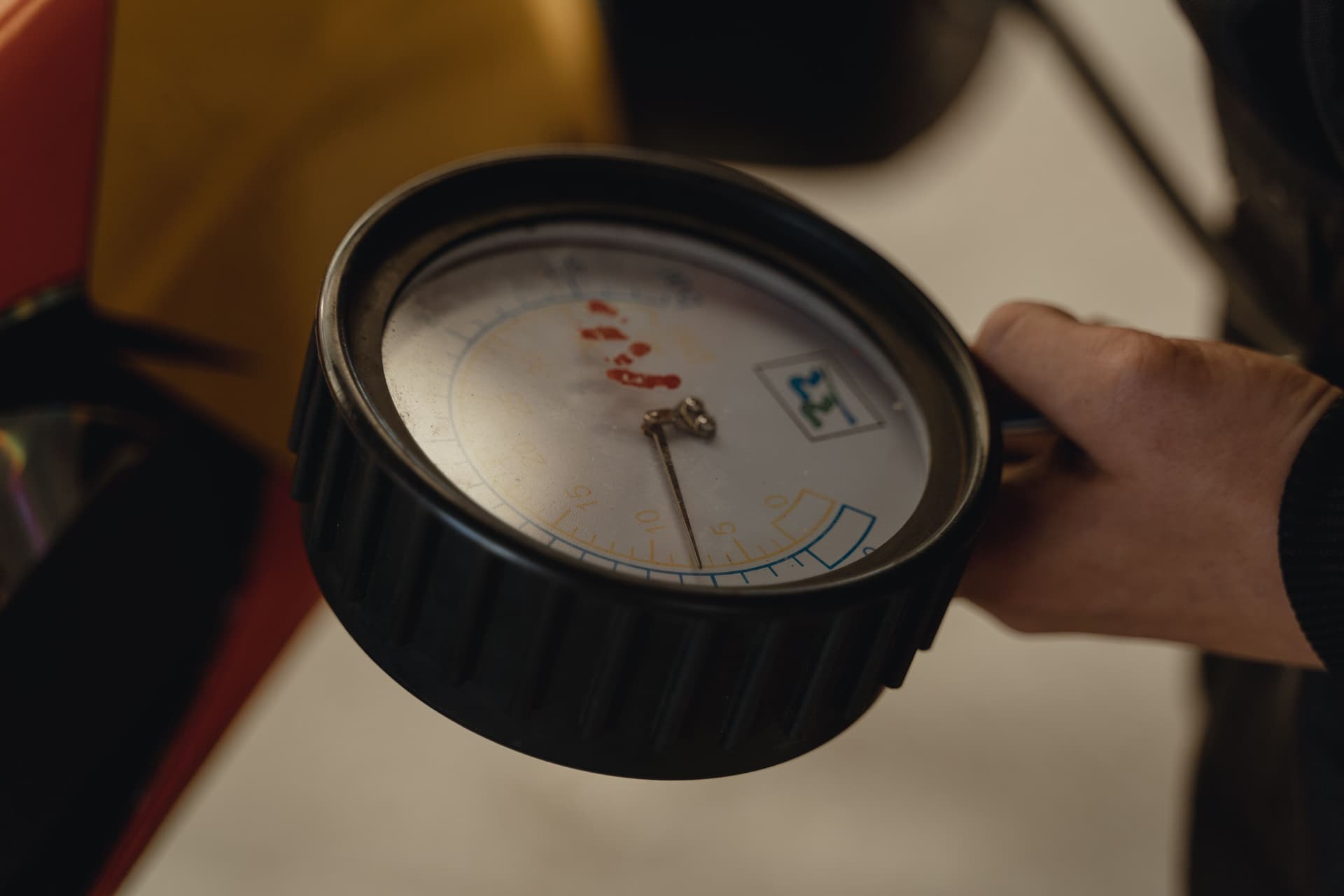 A hand holding a round analog pressure gauge, seen close up