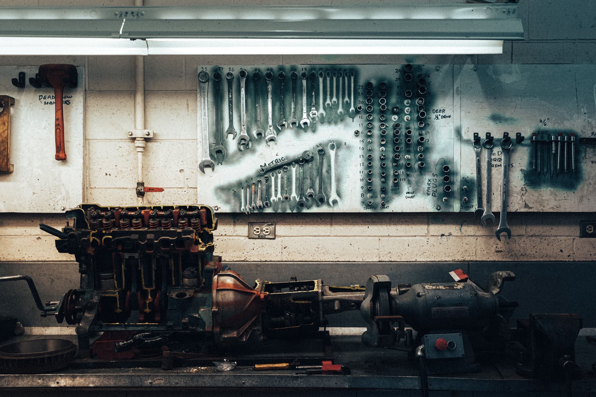 A workshop bench with tools on it and a row of wrenches hanging on a board on the wall above